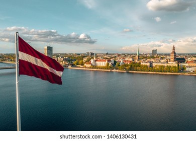 Latvian flag waving in the blue sky with an old town in the background.