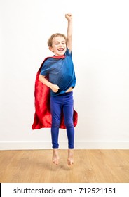 Laughing Active 6-year Old Child Reaching High Like A Joyful Super Hero, Jumping, Reaching Success Over White Background And Wooden Floor, Indoor