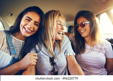 Laughing affectionate female friends riding in the back of a car on a road trip together smiling happily with enjoyment and pleasure at the camera - Shutterstock ID 496220779