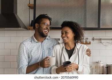 Laughing affectionate young African American family couple drinking morning coffee, standing in modern kitchen, talking speaking joking on weekend at home, spending leisure carefree time together. - Powered by Shutterstock