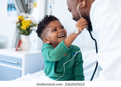Laughing african american boy patient taking male doctor's stethoscope in hospital. Hospital, medical and healthcare services. - Shutterstock ID 2262625615