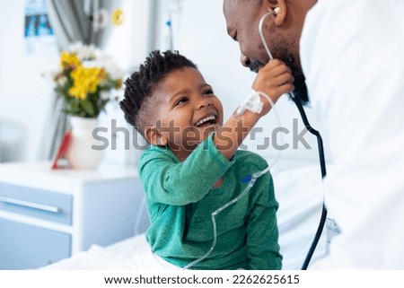 Laughing african american boy patient taking male doctor's stethoscope in hospital. Hospital, medical and healthcare services.
