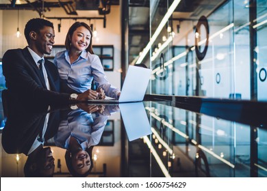 Laughing African American businessman and Asian female colleague watching together funny content on laptop while sitting at reflective counter in office - Shutterstock ID 1606754629