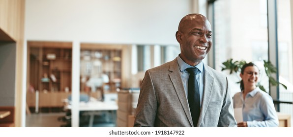 Laughing African American businessman walking in an office holding paperwork after a meeting with colleagues  - Shutterstock ID 1918147922