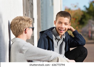 Laughing African American Teen With Braces Sitting Outside With Blond Friend