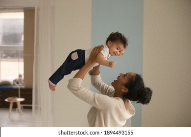 Laughing African American young mother playing with cute little daughter, holding funny baby pretending flying, loving happy mum lifting adorable toddler girl, having fun together at home - Powered by Shutterstock