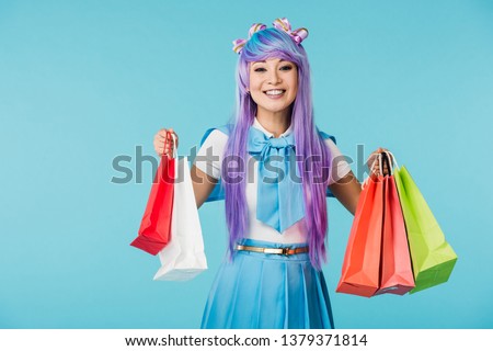 Laughing asian anime girl holding shopping bags isolated on blue