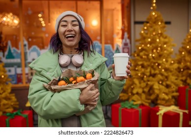 Laughing Asian Girl With Coffee In A Disposable Cup With A Bag Of Tangerines On The Streets Decorated For Christmas