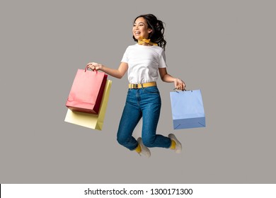 Laughing Asian Woman Holding Colorful Shopping Bags And Happily Jumping Isolated On Grey