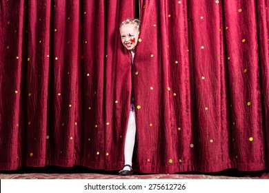 Laughing Attractive Young Blond Girl In Colorful Makeup Making Her Entry On Stage During A Play Or Pantomime Stepping Through The Closed Curtains