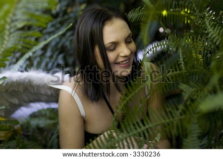 Laughing beautiful brunette fairy sitting in lots of green plants looking away