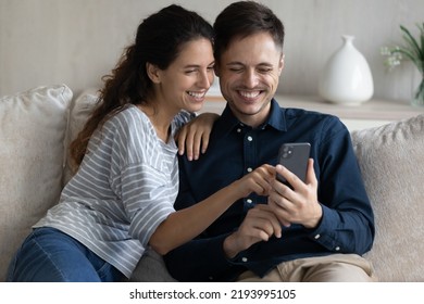 Laughing Beautiful Millennial Latin Married Couple Using Cellphone, Choosing Goods In Internet Shopping Store, Playing Online Games Or Watching Funny Photo Video Content, Modern Technology Addiction