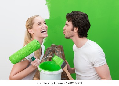 Laughing beautiful woman with a paint roller reacting with merriment to her husband who is standing puckering up his lips for a kiss as they decorate the house together - Shutterstock ID 178015703