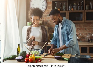 Laughing Black Couple Preparing Healthy Salad Together In Loft Kitchen. Young Family Cooking Dinner