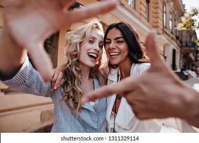 Laughing blithesome woman with dark hair walking down the street with friend. Carefree blonde girl posing on city background. - Powered by Shutterstock