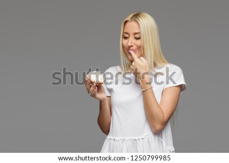 Laughing blond woman eating cake isolated on a grey background. No diet