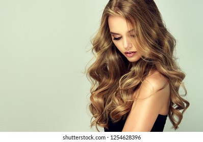 Laughing blonde girl with long  and   shiny wavy hair .  Beautiful  smiling woman model with curly hairstyle .