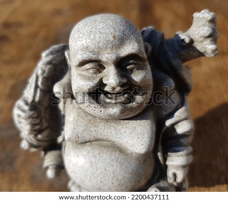 Laughing Buddha (Hotei) - a gray ceramic figurine in the sun, on a brown wooden background (macro, full face, upper part of the figure).