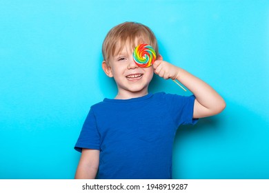 Laughing Caucasian child kid boy close one eye bright colorful lollipop candy. Close-up studio shot on blue background. - Powered by Shutterstock