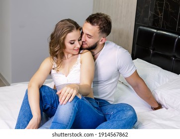 Laughing cheerful family embracing on bed indoors, wearing casual outfits. Attractive young boyfriend embracing his girlfriend on couch at home. Happy couple in love in the weekend evening. Weekend