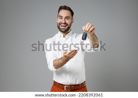 Laughing cheerful funny young bearded business man 20s wearing classic white shirt stand pointing hand on car keys isolated on grey color background studio portrait. Achievement career wealth concept