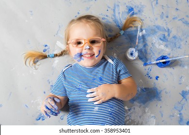 Kinder mit blauen Farbpunkten auf dem Gesicht mit Farben und Pinseln auf dem Boden lachen.