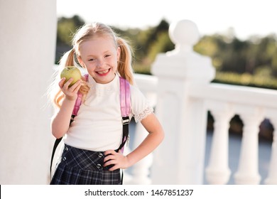 Laughing Child Girl 5-6 Year Old Eating Green Fresh Apple Outdoors. Wearing School Backpack And Uniform. Childhood. Back To School. 1 September. Good Morning. 