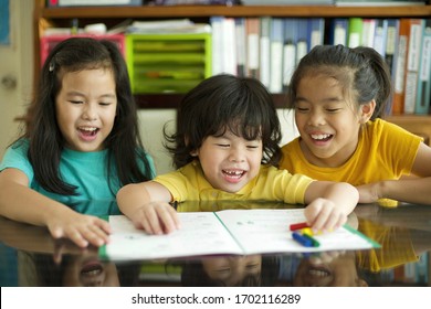 Laughing Children Doing Homework.Cheerful Girls And A Boy Learning Together.Siblings Home Education.Boy Preschooler With Sisters.Group Study.Elementary And Preschool Students.Math Lesson Workbook.