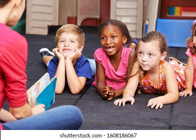 Laughing Children In Kindergarten Listen To A Story While Reading Aloud