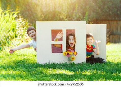 Laughing Children Play In The House Made Of Cardboard Box. Little Boy And Girl Dream About New Home And Family.