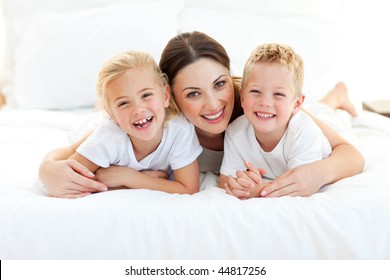 Laughing Children Playing With Their Mother Lying On A Bed At Home