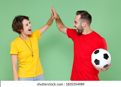 Laughing Couple Friends Sport Family Woman Man Football Fans In Yellow Red T-shirts Cheer Up Support Favorite Team With Soccer Ball Giving High Five Holding Hands Folded Isolated On Green Background