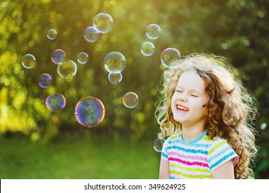 Laughing curly girl with bubbles. Happy childhood concept.