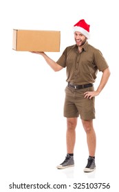 Laughing Delivery Man In Santa Claus Hat On The Phone, Standing And Holding Carton Box On One Hand. Full Length Studio Shot Isolated On White.