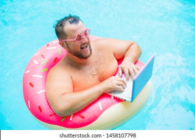 laughing Fat funny man in pink inflatable circle in pink glasses works on a laptop in a swimming pool. - Shutterstock ID 1458107798