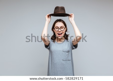 Laughing Female nerd in eyeglasses holding overhead her hat and looking at camera