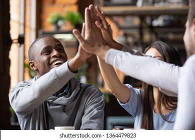 Laughing friends sitting in cafe spends time together feels happy giving high five hand gesture. Concept of equality and friendships of different ethnicity millennial people, unity warm relationships