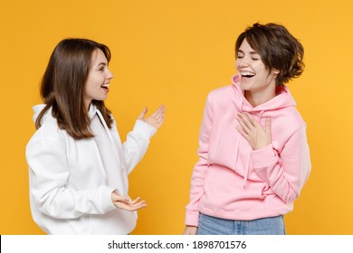 Laughing Funny Two Young Women Friends 20s Wearing Casual White Pink Hoodies Standing Speaking Talking Spreading Hands Looking At Each Other Isolated On Bright Yellow Color Background Studio Portrait