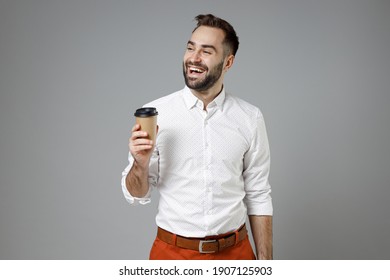 Laughing Funny Young Bearded Business Man In Classic White Shirt Standing Hold Cup Of Coffee Or Tea Looking Aside Isolated On Grey Color Background Studio Portrait. Achievement Career Wealth Concept