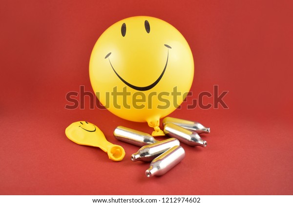 Laughing gas bombs stock images. Laughing gas balloons. Happy emoji balloon. Smiley inflatable balloon isolated on a red background. Laughing party balloon. Nitrous oxide bulbs