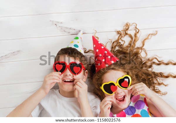 Laughing girl and boy with sunglasses, hold candles heart form, lying on the wooden floor. Christmas, New Year or Valentines day concept.