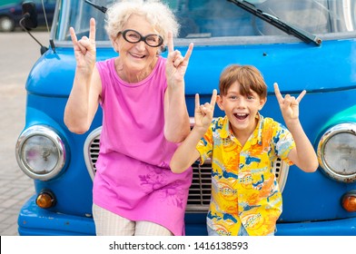 Laughing Grandmother With Her Grandson In Summer Beachwear Near A Retro Car Show Two Fingers Up. Family Summer Vacation And Travel Concept