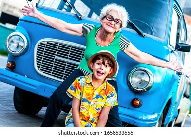 Laughing Grandmother With Her Grandson In Summer Beachwear Near A Retro Car Have Fun. Family Summer Vacation And Travel Concept