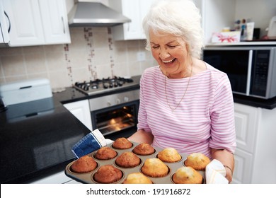 A laughing grandmother holding a tray of baked muffins just out of the oven - Powered by Shutterstock