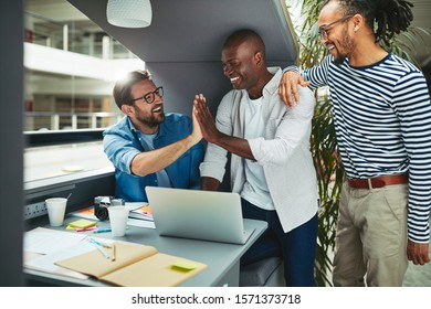 Laughing Group Of Diverse Creative Professionals High Fiving Each Other While Working On A Laptop Together In An Office Meeting Pod