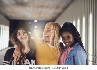 Laughing group of diverse young girlfriends having fun while walking together down a walkway in the city at night - Shutterstock ID 1016842654