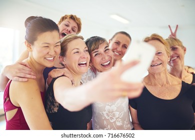 Laughing group of senior women standing arm in arm together taking a selfie with their dance teacher during ballet class - Powered by Shutterstock