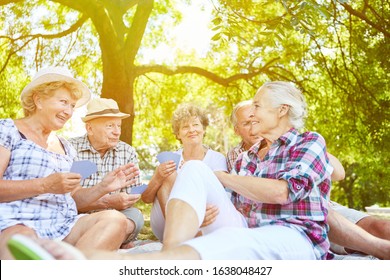 Laughing Group Of Seniors Playing Cards In The Garden In Summer