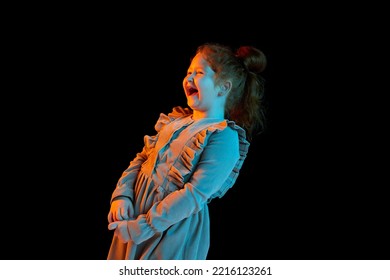 Laughing. Half-length portrait of cute cheerful little girl wearing festive dress isolated over dark background in neon light. Concept of kids emotion, facial expressions, fashion. Happy childhood - Shutterstock ID 2216123261