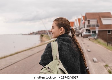 Laughing Happy Brunette Woman Walking Outdoor With Backpack On Her Shoulder, Tourist Woman. Rear View Of Woman Wit High Ponytail With Braid Look At Back And Smiling. Travel, Trip, Vacation Concept.